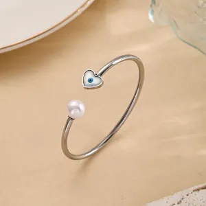 Detail of silver open bangle with a white pearl and heart-shaped evil eye charm