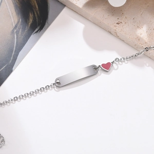 Détail d'un bracelet d'identité en acier avec breloque cœur rouge et plaque à graver