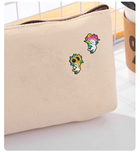 Close-up of cute enamel cat pins with flowers pinned on a beige canvas tote bag