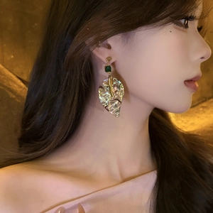 Close-up of leaf earring with pearlescent finish, gold trim and green gemstone detail