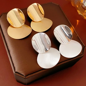 Close-up of gold and silver brushed metal oval drop earrings on a leather surface