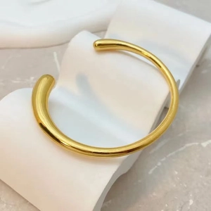 Bracelet manchette minimaliste plaqué or 18K avec finition polie sur support moderne