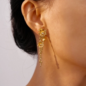 Close-up of gold flower drop earrings with rhinestones on a female model