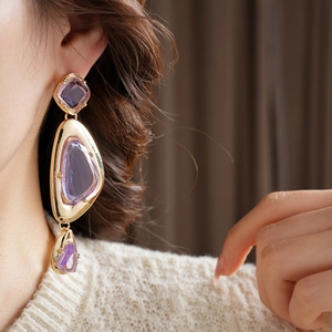 Close-up of vintage gold earrings with purple geometric stones and irregular tassels