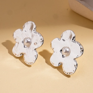 Macro detail of silver flower stud earrings with hammered texture and white pearl center