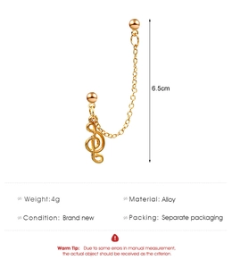 Detailweergave asymmetrische gouden oorbel met muzieknoot, lange ketting en legering afwerking