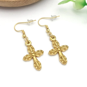 Detailed close-up of golden cross earrings with textured leaf pattern on white background