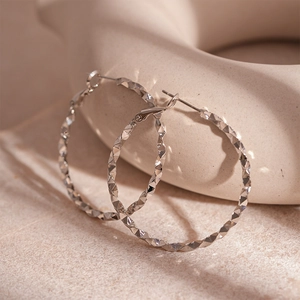 Macro detail of silver geometric hoop earrings with reflective faceted diamond cut texture