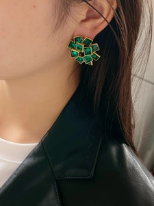 Detail of square emerald green crystal flower earrings worn with a chic leather jacket