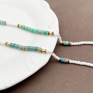 Macro shot of minimalist beaded bracelet with turquoise stones and gold metal accents