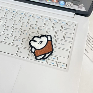 Close-up of a white embroidered cartoon bear pin placed on a white laptop keyboard