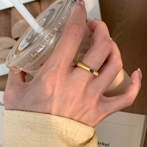Close-up of a vintage brushed gold ring featuring a green emerald gemstone on finger