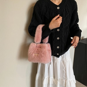 Pink plush bucket bag with metal nameplate worn by model in black knit cardigan