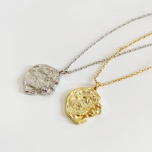 Irregular textured coin pendant necklace in gold and silver finishes on light background