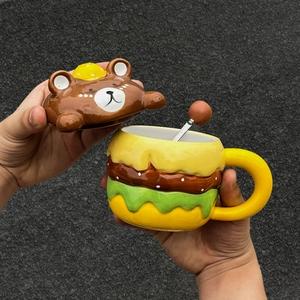 Close-up of burger shaped ceramic mug with bear head lid held in hands outdoors