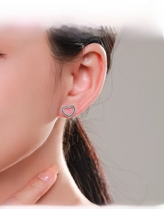 Close-up of retro hollow heart stud earrings with milgrain edges worn by a model