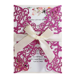 Detail of pink glitter laser cut wedding invitation with white ribbon and floral card