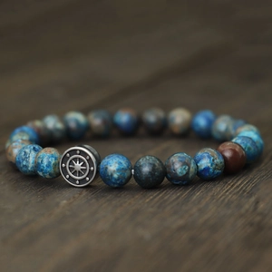 Macro shot of natural stone beaded bracelet with a silver compass charm on dark wood