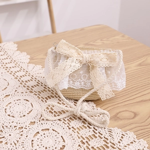 Detail of a straw crossbody bag with white lace overlay and large yellow bow
