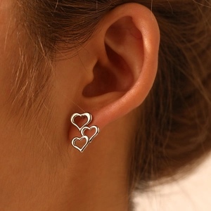 Detailed view of silver triple hollow heart earrings worn on ear showing tiered design