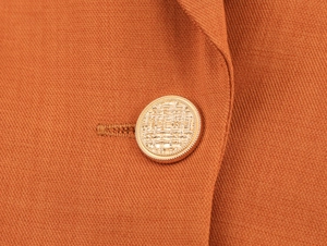 Close-up of golden textured button on orange blazer with visible twill fabric detail
