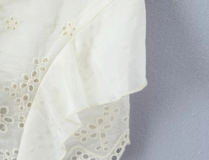 Detail of white camisole top featuring hollow embroidery and layered ruffle design