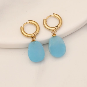 Detail of gold huggie earrings featuring blue translucent charms with cross inlay