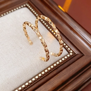 Macro shot of gold geometric C-shaped earrings on a beige fabric background