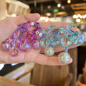 Handheld view of four colorful faceted cherry hair ties in purple and teal blue colors