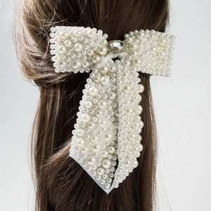 Elegant bridal hair bow clip with white pearls and sparkling rhinestone center on dark hair