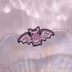 Detailed close-up of a purple bat enamel pin featuring 'YOU SUCK' text in punk style