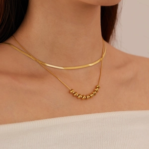 Double-layered gold titanium steel necklace featuring a snake chain and beaded strand on a model