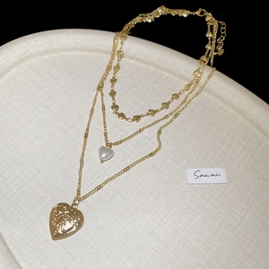 Close-up of triple-layered gold necklace featuring heart pendants and pearl accents