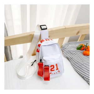 Détail d'un sac de poitrine blanc pour enfants avec lettrage orange sur un lit