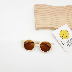 Detail view of retro round-frame kids sunglasses in off-white on a minimalist white setting