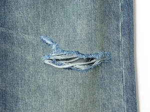 Close-up of distressed ripped details and denim texture on blue mid-waist jeans