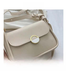 Detail of a beige flap crossbody bag featuring a round gold magnetic buckle and stitching