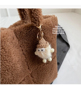 Nahaufnahme eines weißen Plüsch-Monsteranhängers mit brauner Strickmütze an einer Tasche