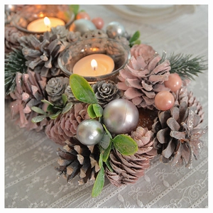 Close-up of a Christmas candle holder with pine cones, pink ornaments and a glass cup