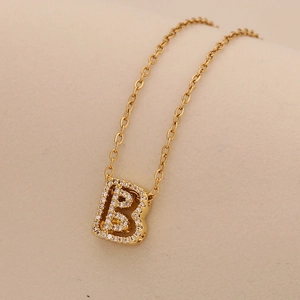 Macro shot of gold letter B pendant necklace with sparkling zircon on beige backdrop