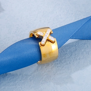 Macro shot of gold-plated X-shaped cross ring with pavé zircons on blue textured ribbon