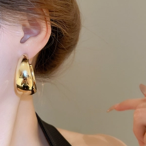Close-up of a large gold polished chunky C-shaped hoop earring worn by a model