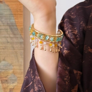 Detailed macro of a vintage gold-plated tassel bangle with multicolored beads and droplets