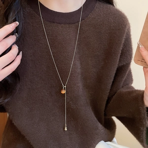 Close-up of a gold Y-shaped necklace with tiger eye beads on a brown sweater