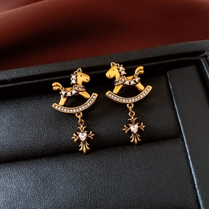Detail of gold horse earrings with white zircon pavé and heart-shaped cross pendant