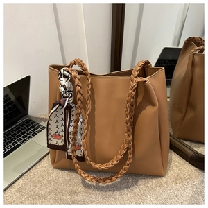 Détail du sac cabas marron clair avec poignées tressées et foulard sur un tapis doux