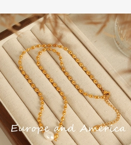 Detailed shot of a gold bean chain necklace with white baroque pearl on velvet display