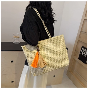 Detail view of beige straw tote bag with vibrant orange and khaki fringe tassel charm
