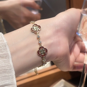 Détail d'un bracelet trèfle doré avec émail rouge et cristaux porté sur un poignet féminin