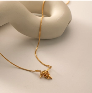 Detail view of a gold knot pendant on a delicate chain draped over a ceramic sculpture